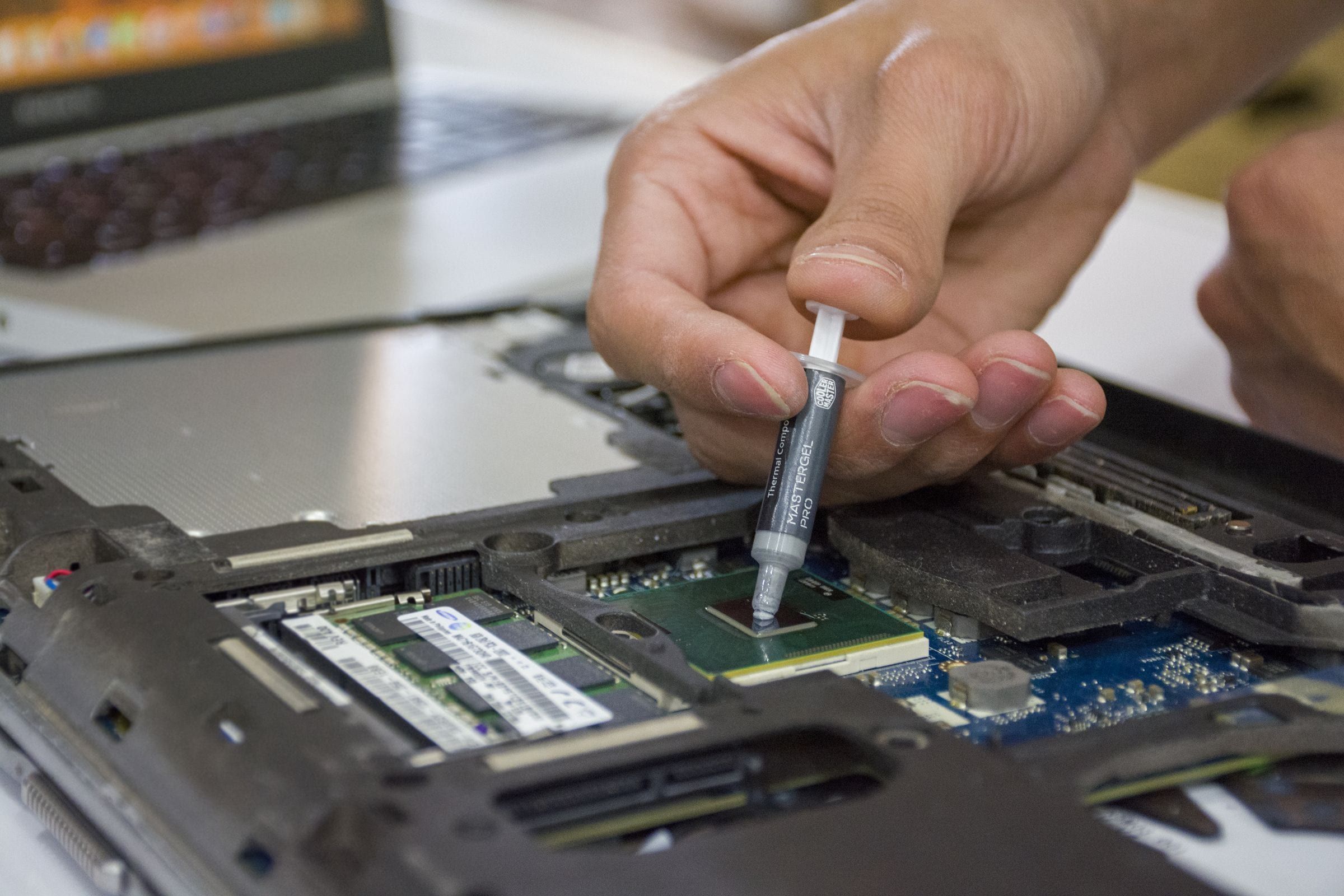 Mano aplicando pasta térmica con una jeringa sobre el procesador de una notebook abierta