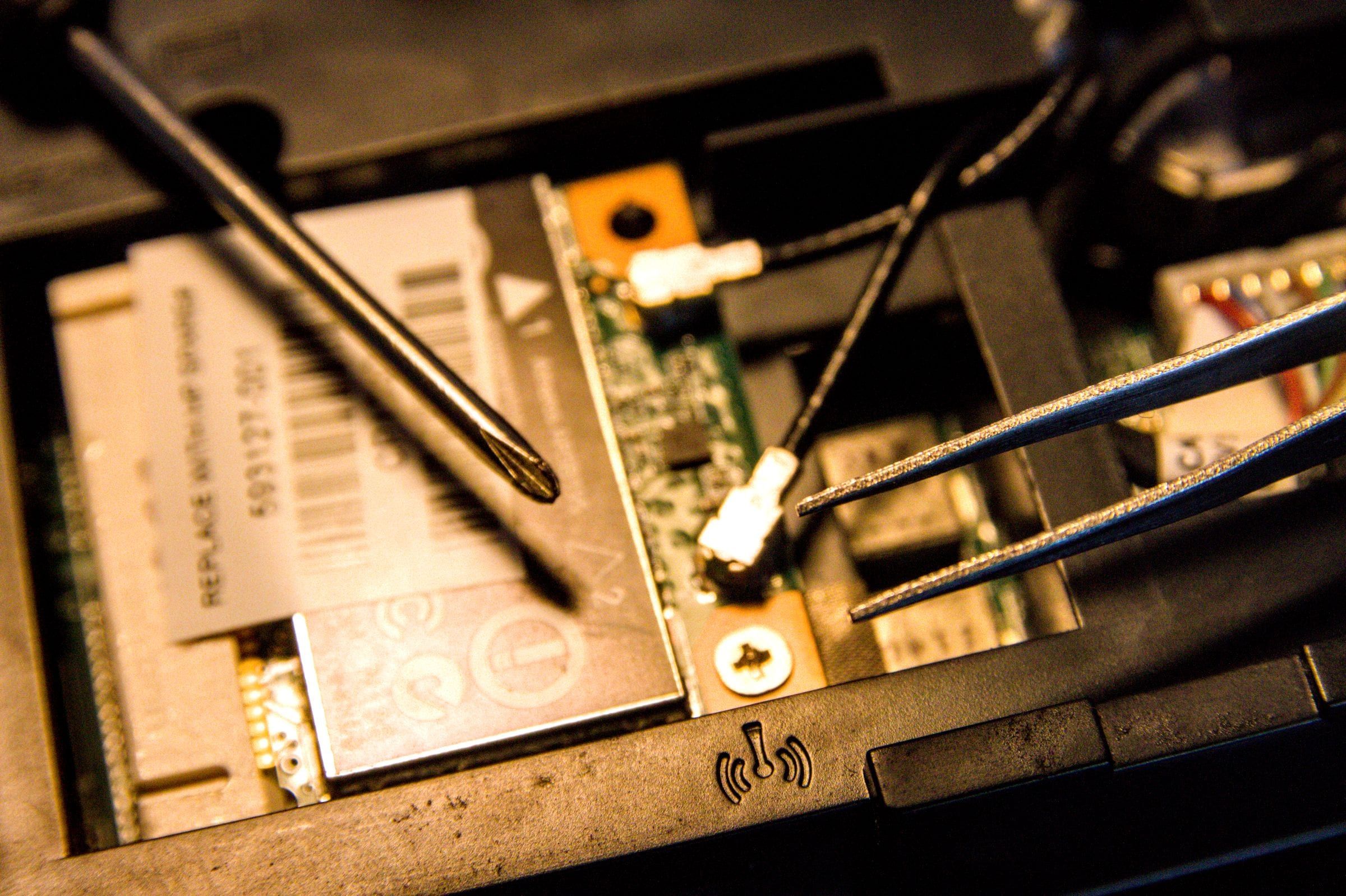 Primer plano del interior de una notebook con un destornillador y una pinza apoyados sobre la placa wifi