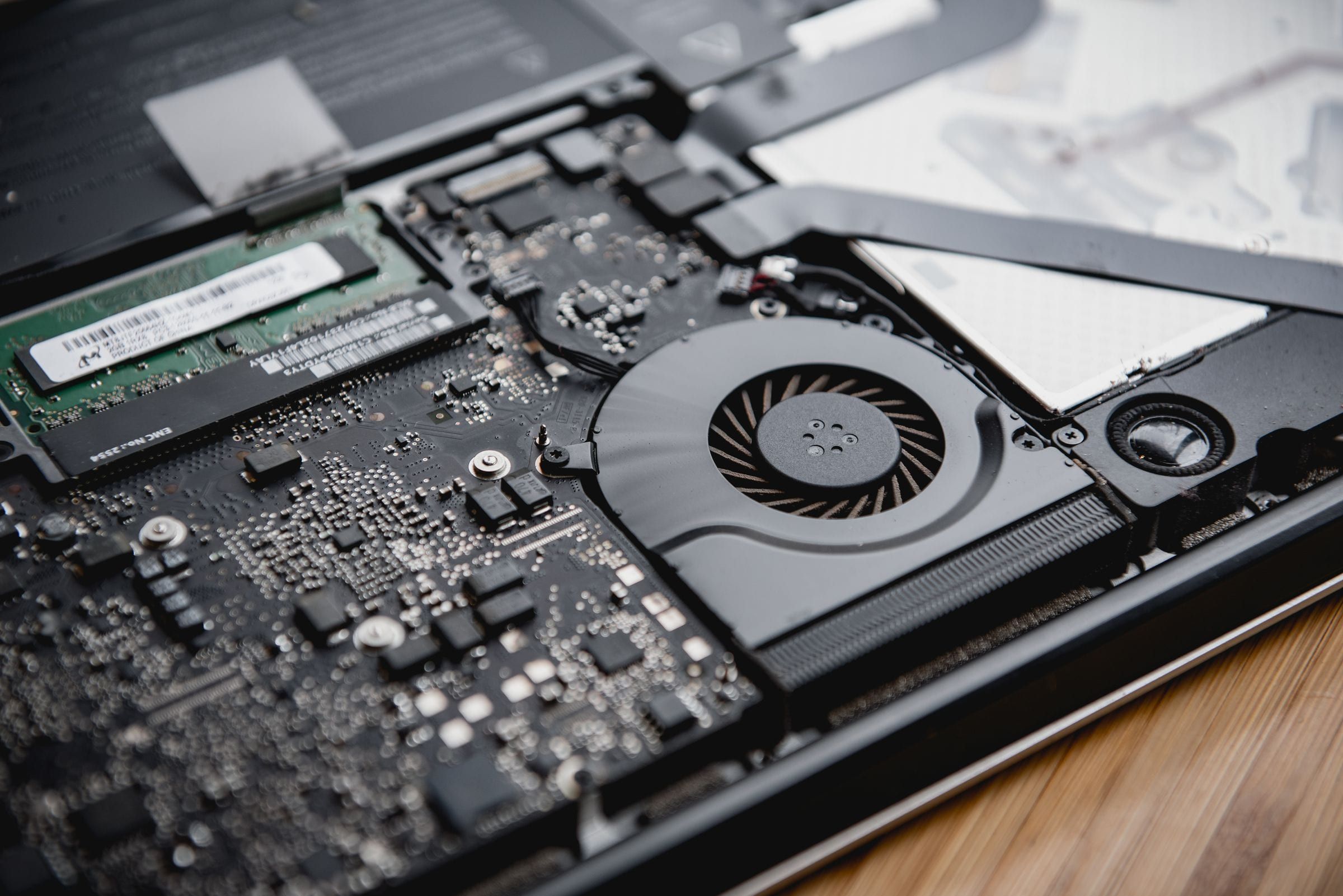 Notebook sin la tapa inferior sobre una mesa de madera, con el ventilador, la memoria y la placa a la vista