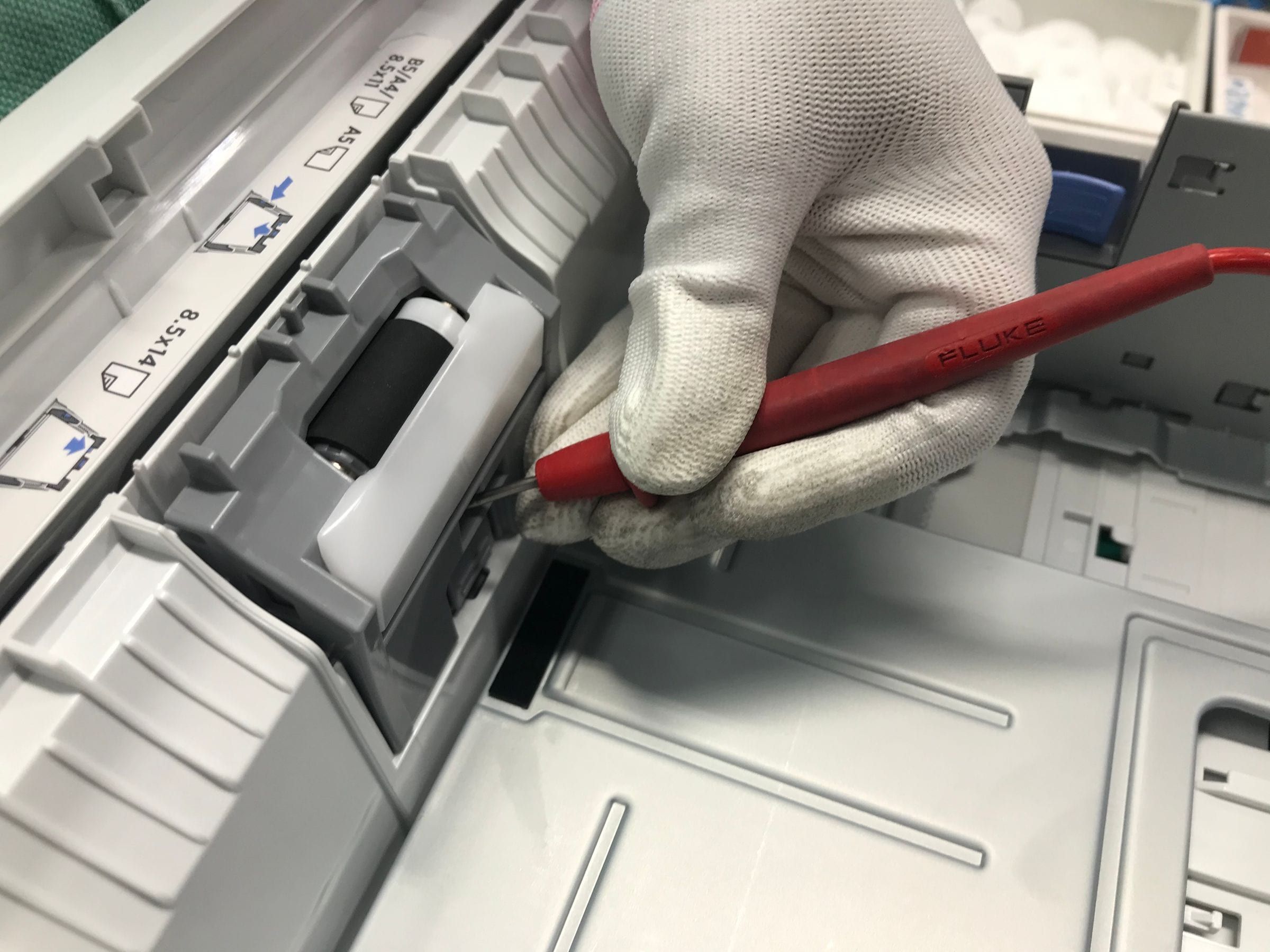 Mano con guante reparando el rodillo de la bandeja de papel de una impresora