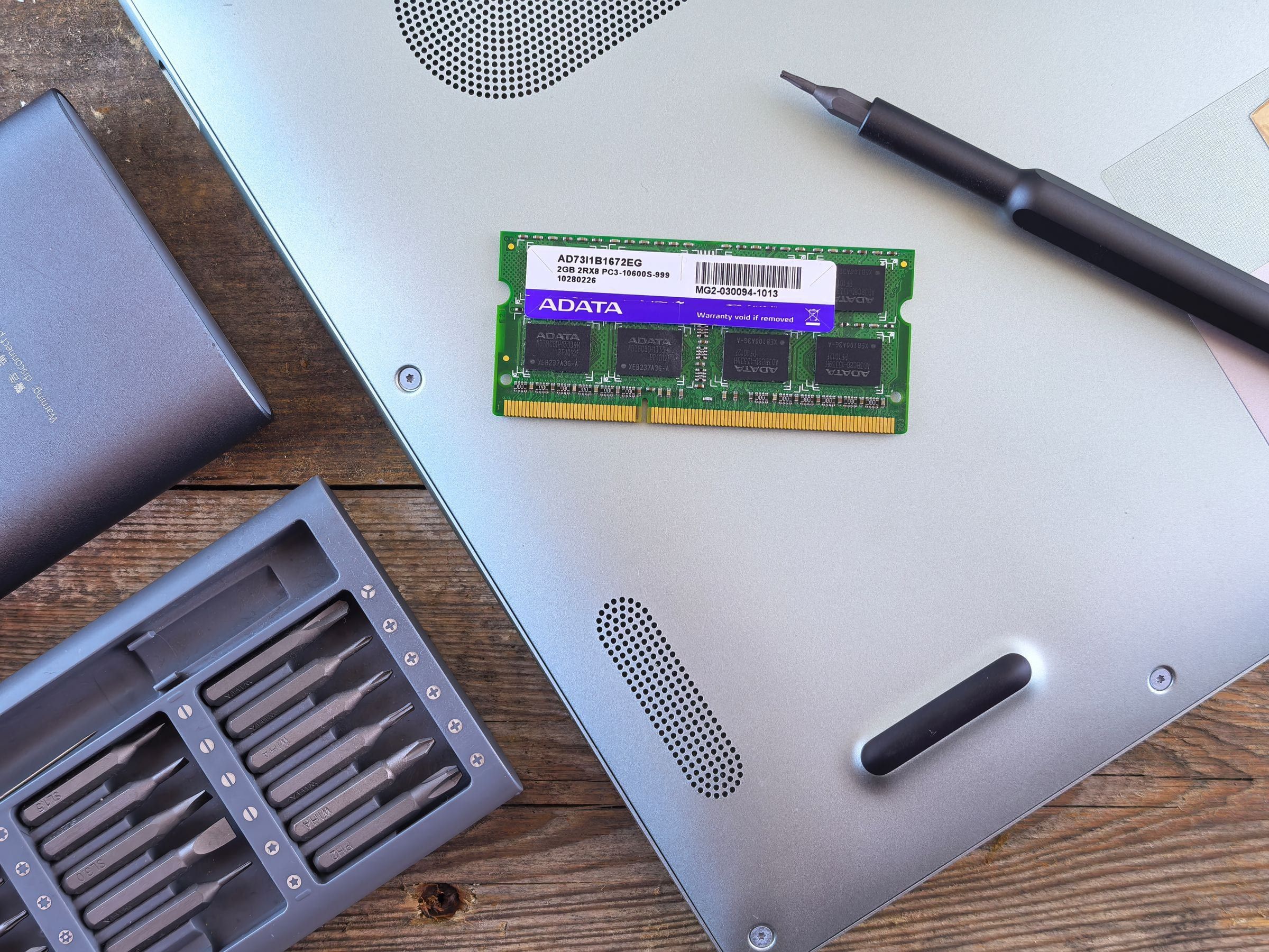 Módulo de memoria RAM apoyado sobre la base de una notebook, junto a un set de puntas y un destornillador